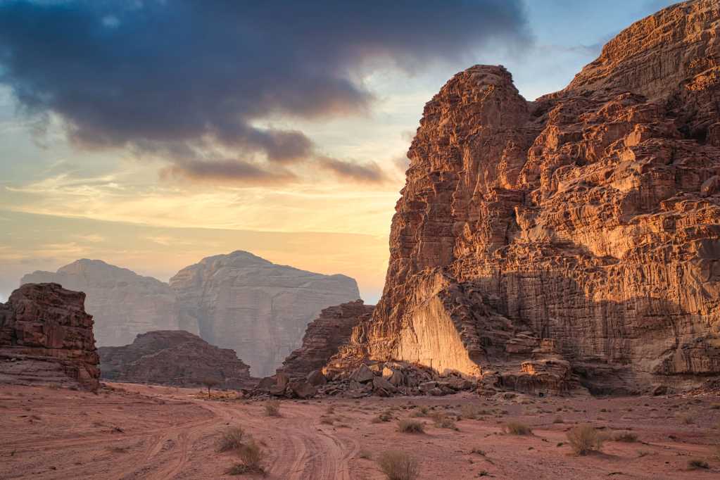 A breathtaking sunset over the red sandstone cliffs and orange desert dunes of Wadi Rum, Jordan, captured by Natasha Bishop.